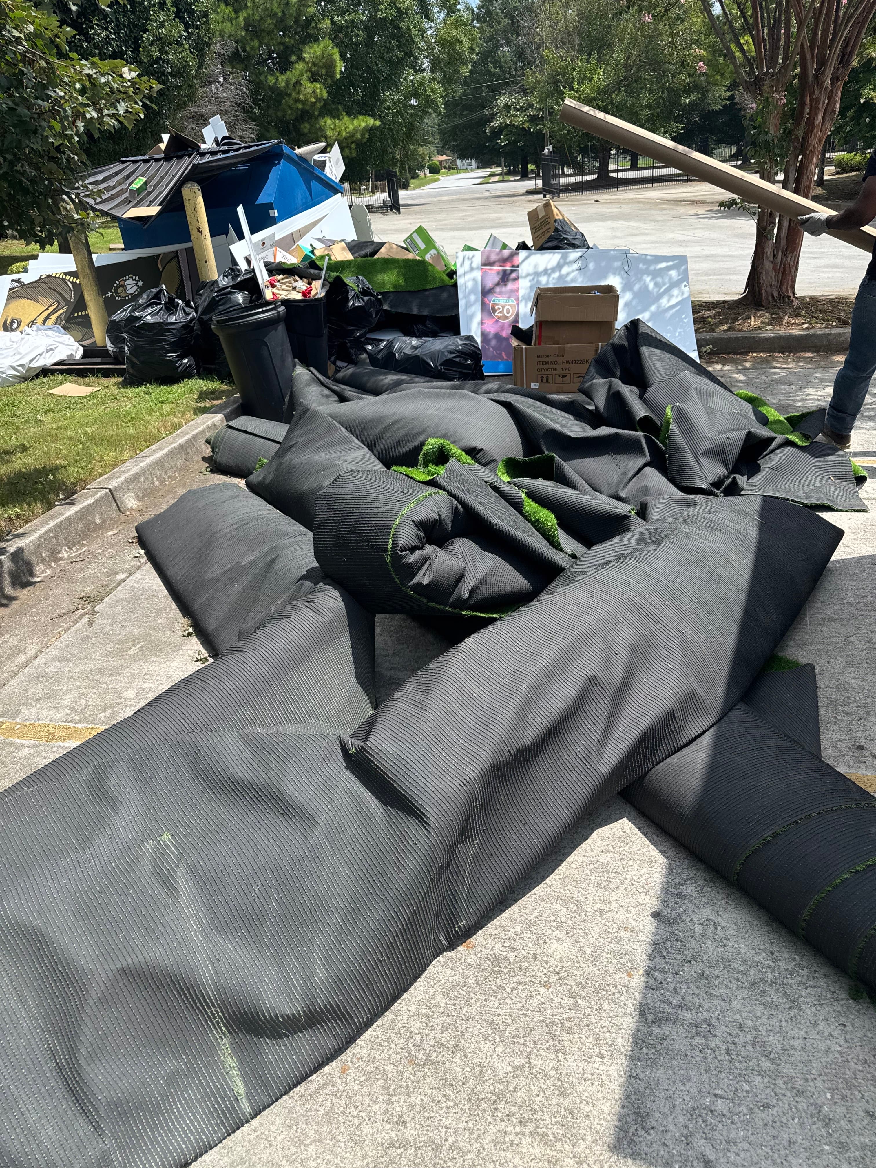 Commercial cleanup with large rolls of carpet, bags, and renovation debris staged for removal near a dumpster area.